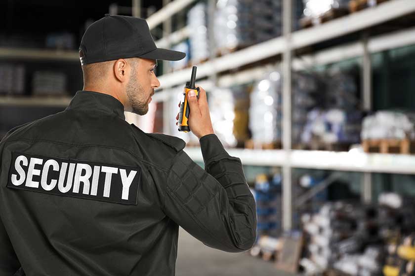 Security guard using portable radio transmitter in wholesale warehouse, space for text